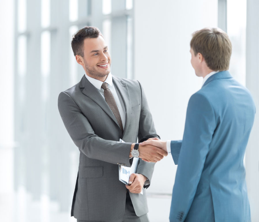 Two men in suits shaking hands and smiling.